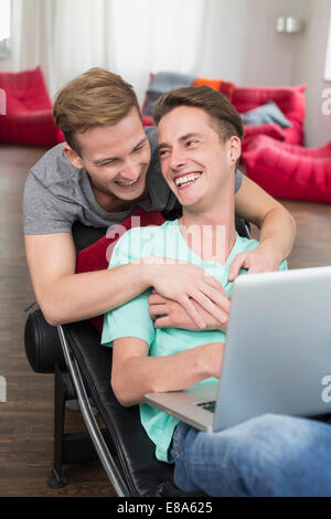 Homosexuelles Paar mit Laptop im Liegestuhl, Lächeln Stockfoto