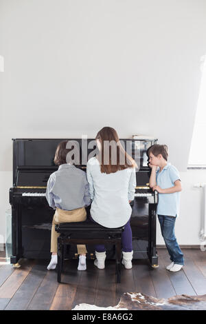 Mutter und Tochter, Klavier zu spielen, während Bruder hört Stockfoto