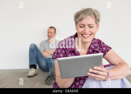 Reife Frau mit digital-Tablette während der Reife Mann sitzt im Hintergrund Stockfoto