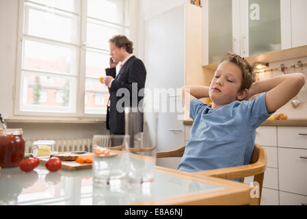 Gelangweilte junge in Küche mit Vater am Telefon im Hintergrund Stockfoto