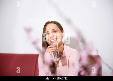 Junge Frau Sofa sitzen lächelnd Trinkwasser Stockfoto