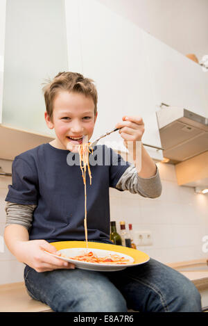 Junge Essen Spaghetti auf Küchentisch Stockfoto