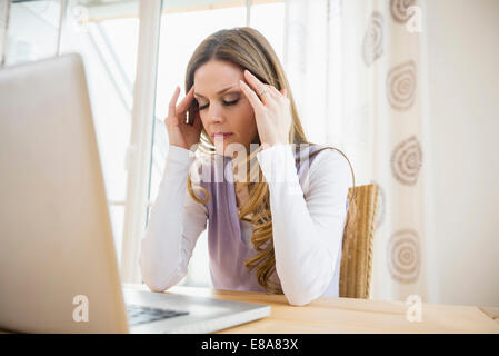 Schwere Frau mit Kopf in der hand mit Laptop zu Hause Stockfoto