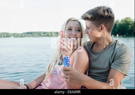 Teenager-paar Seifenblasen auf einem Steg am See Stockfoto