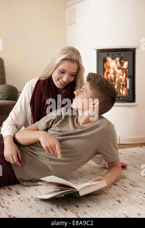 Teenager-Paar mit Buch liegend auf Teppich vor Kamin Stockfoto