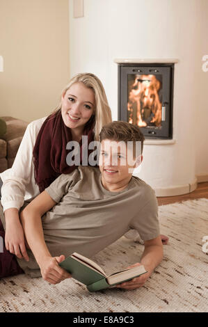 Teenager-Paar mit Buch liegend auf Teppich vor Kamin Stockfoto