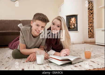 Teenager-Paar mit Buch liegend auf Teppich vor Kamin Stockfoto