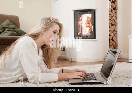 Teenager-Mädchen mit Laptop auf Teppich vor dem Kamin liegen Stockfoto