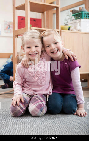 Zwei lächelnde Mädchen, beste Freunde, sitzen am Boden im kindergarten Stockfoto