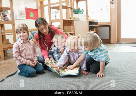 Weibliche Erzieher und vier Kinder sitzen am Boden des Kindergartens Bilderbuch betrachten Stockfoto
