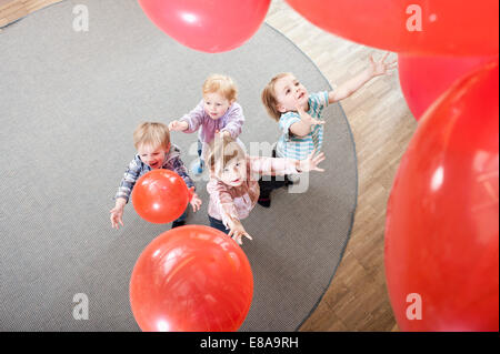 Vier Kinder, die spielen mit roten Luftballons in Kindergarten, erhöht, Ansicht Stockfoto