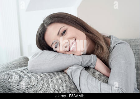 Porträt der lächelnde junge Frau auf Couch zu Hause Stockfoto