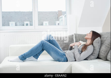 Junge Frau mit geöffneten Buch auf Couch zu Hause Stockfoto