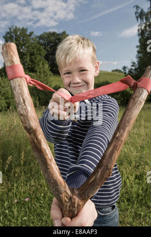 Kleiner Junge hält hölzerne Schleuder lächelnd Stockfoto