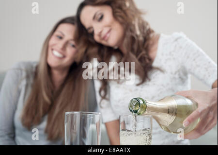 Junge Frau gießt Champagner in Gläser während ihre Freundin beobachten Stockfoto