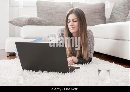 Porträt der jungen Frau mit Laptop auf Teppich zu Hause liegen Stockfoto