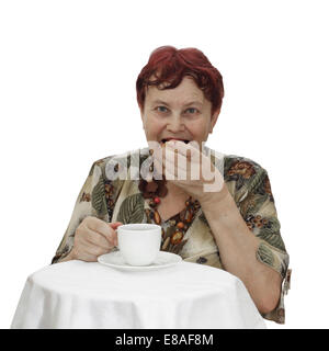 Ältere Frau sitzt am Tisch mit Tasse Tee und Essen Cookie isoliert auf weißem Hintergrund Stockfoto