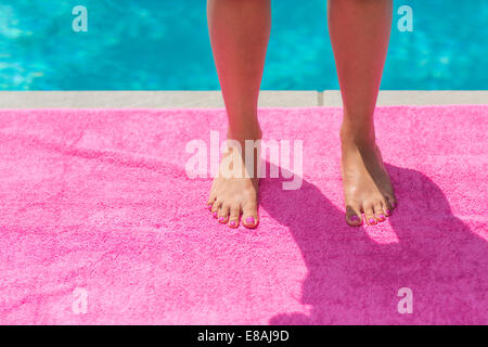 Zugeschnittenen Schuss der jungen Womans Beine und Füße stehen auf Rosa Strand Handtuch am Pool Stockfoto