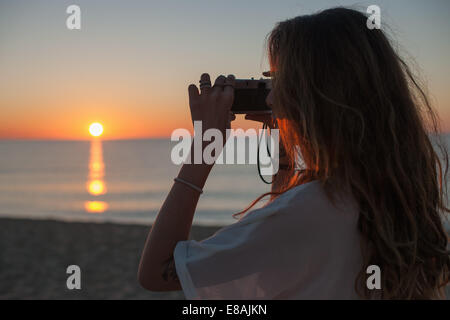 Junge Frau auf der Suche durch ein Fernglas bei Sonnenuntergang am Strand, Castiadas, Sardinien, Italien Stockfoto