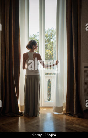 Elegante junge Frau aus dem Wohnzimmer Fenster suchen Stockfoto