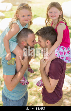 Zwei Schwestern sitzen auf beiden Schultern der Väter im park Stockfoto