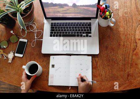 Person schriftlich Tagebuch mit Laptop am Schreibtisch Stockfoto