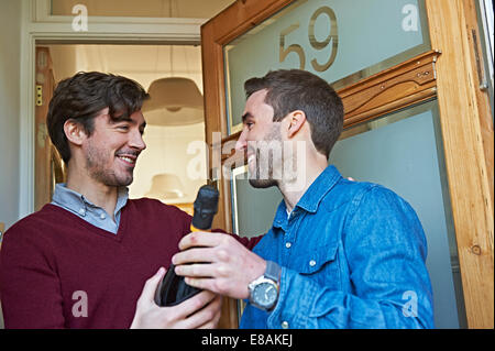 Männer mit Flasche Wein lächelnd an Haustür Stockfoto