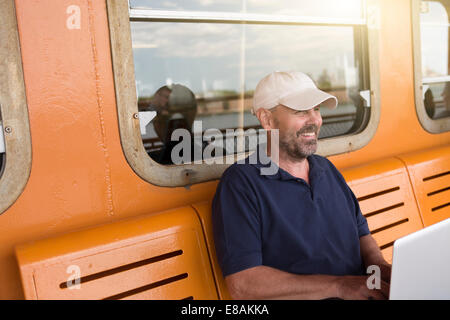 Reifer Mann mit Laptop auf Passagier-Fähre Stockfoto