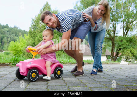 Mitte erwachsenes paar schob Baby Tochter auf Spielzeugauto im Garten Stockfoto