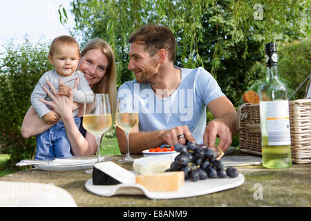 Mitte erwachsenes paar und Tochter sitzen an Picknick-Tisch im Garten Stockfoto