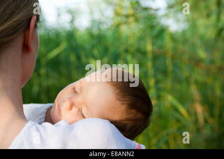 Über Schulter Porträt von Mitte Erwachsene Mutter und schlafenden Baby Tochter im Garten Stockfoto