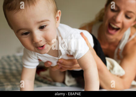 Mutter guiding Babyjungen kriechen auf Bett Stockfoto