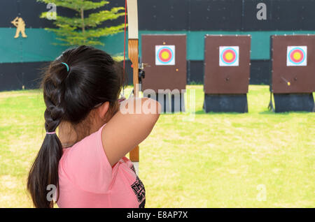 Junges Mädchen halten und mit dem Ziel Bogen im Übungsfeld Stockfoto