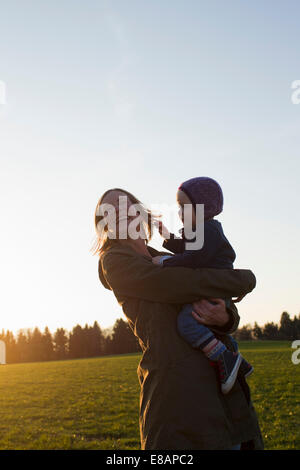 Reife Mutter und Baby Tochter lachend im Feld bei Sonnenuntergang Stockfoto