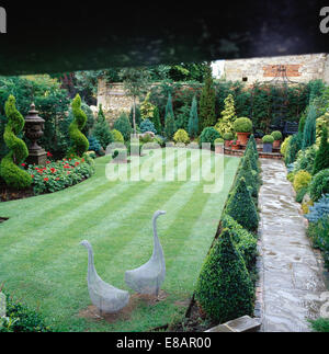 Zwei Kabel Arbeit Gans Statuen auf Rasen umgeben von Formschnitt in gut gepflegt ummauerten Garten mit gepflasterten Weg Stockfoto