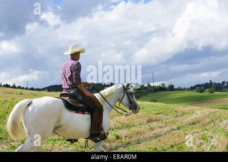 Junger Mann in Cowboy-Ausrüstung-Reiten in Feld Stockfoto