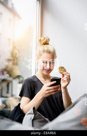Junge Frau, Lesen von Texten auf Smartphone in Fensterplatz Stockfoto