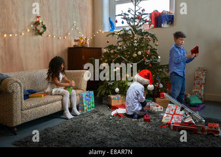 Mädchen und zwei Brüder Weihnachtsgeschenke im Wohnzimmer öffnen Stockfoto