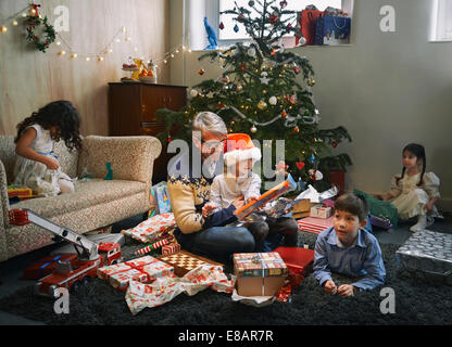 Vater und seinen vier Kindern Weihnachtsgeschenke im Wohnzimmer öffnen Stockfoto