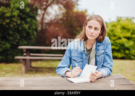 Junge Frau sitzt bei Picknickbank im Park schreiben in notebook Stockfoto