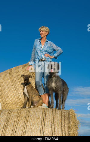 Reife Frau mit zwei Hunden stehen blicken Sie von Heuhaufen Stockfoto