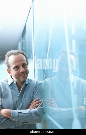 Zuversichtlich reifer Geschäftsmann gelehnt Glaswand im Büro Stockfoto
