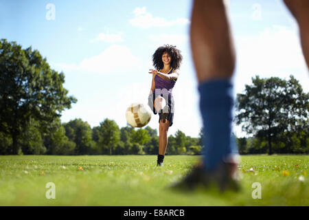 Junge Frau treten Fußball in Richtung Freund im park Stockfoto