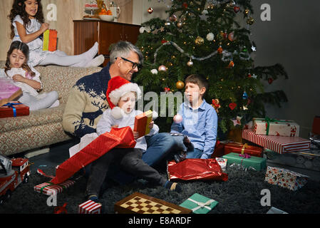 Vater im Wohnzimmer Bodenöffnung Weihnachtsgeschenke mit Kindern Stockfoto