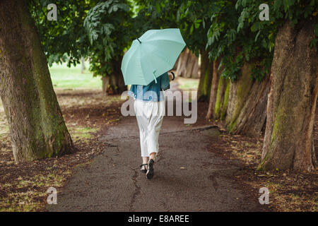 Rückansicht des jungen Frau mit Regenschirm spazieren im park Stockfoto