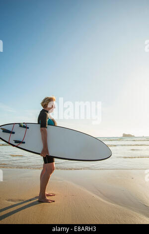 Ältere Frau, die am Strand mit Surfbrett, Camaret-Sur-Mer, Bretagne, Frankreich Stockfoto