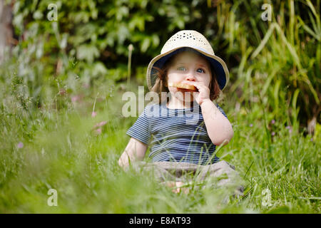 Junges Mädchen sitzen Gras essen snack Stockfoto