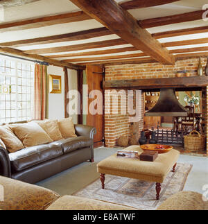 Beige Velours gepolsterte Hocker und Leder Sofa in Holzbalken Ferienhaus Wohnzimmer mit einem großen offenen Kamin Stockfoto