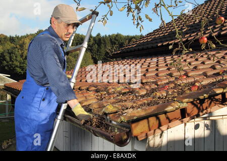 Ein Mann Reinigung ein regen Gosse auf einer Leiter Stockfoto