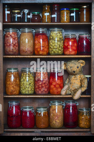 Fadenscheinig One Eyed Teddybär auf einem Holzregal mit gespeicherten in Flaschen Früchte, Marmeladen und Konfitüren Stockfoto